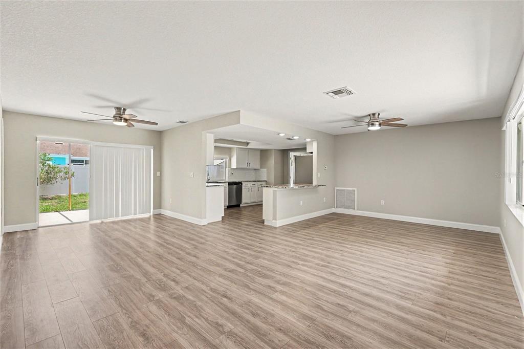 An open-concept living area with light wood-look flooring, ceiling fans, and a kitchen pass-through — 3750 LIGHTHOUSE WAY, HOLIDAY, FL
