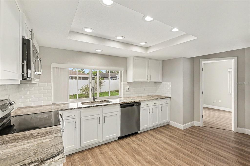 A kitchen with white cabinets, granite countertops, stainless steel appliances, and wood-look flooring — 3750 LIGHTHOUSE WAY, HOLIDAY, FL