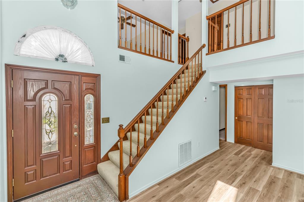 A two-story foyer features a wooden staircase, light wood flooring, and a decorative front door — 5412 RUTLAND COURT, ORLANDO, FL