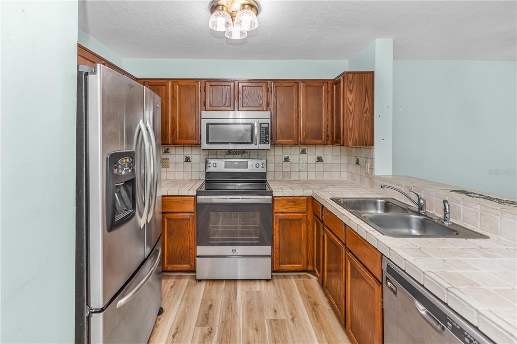 A kitchen features wood cabinets, stainless steel appliances, and tiled countertops with a double sink — 5412 RUTLAND COURT, ORLANDO, FL