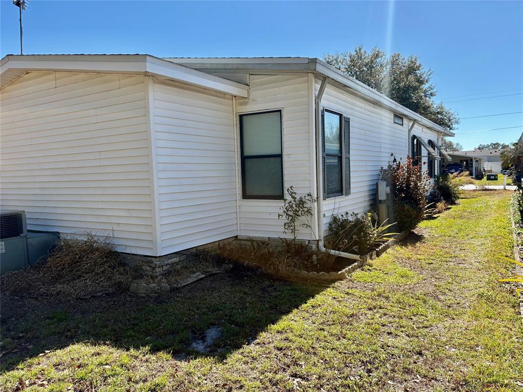The exterior of a white mobile home features horizontal siding and a small garden bed — 6081 SOUTHERN OAKS DRIVE SE, WINTER HAVEN, FL