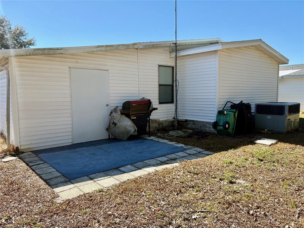 The exterior of a white mobile home features a small patio, a door, and an air conditioner — 6081 SOUTHERN OAKS DRIVE SE, WINTER HAVEN, FL