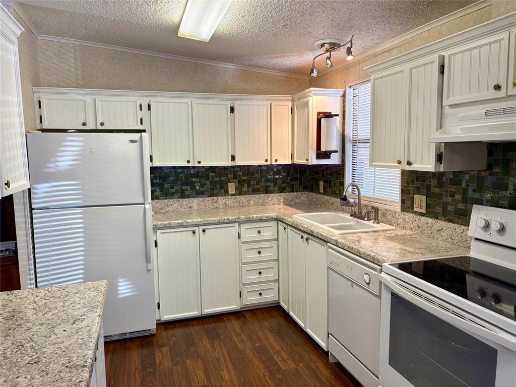 A kitchen features white beadboard cabinets, granite countertops, a tiled backsplash, and white appliances — 6081 SOUTHERN OAKS DRIVE SE, WINTER HAVEN, FL