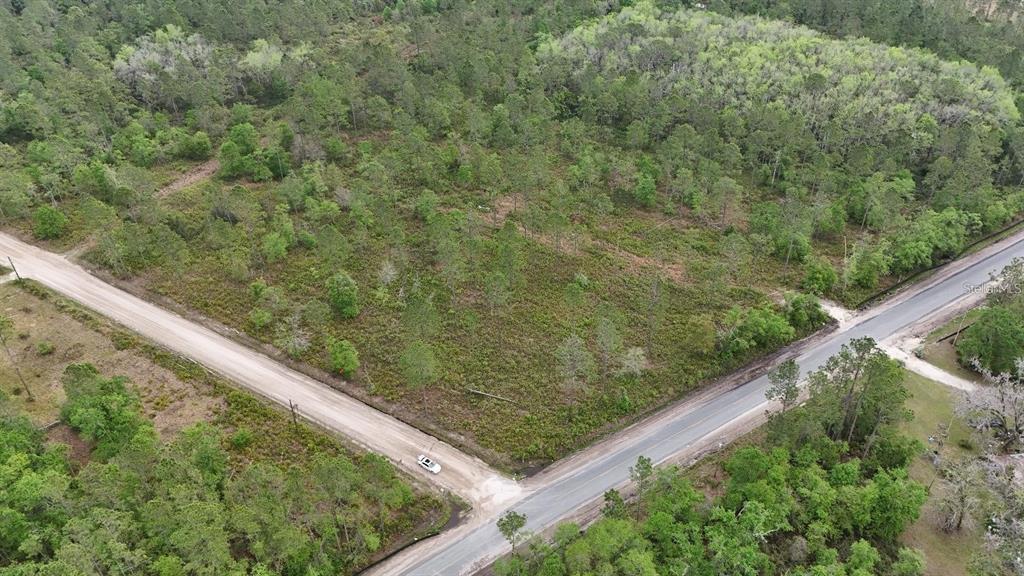 An aerial view shows a wooded, undeveloped corner lot bordered by a paved and dirt road — SE COUNTY ROAD 25A, WHITE SPRINGS, FL