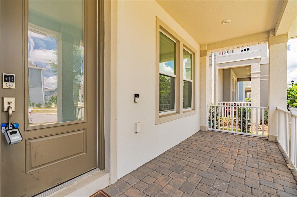 A covered front porch with stone pavers, a tan door, and a white railing — 15010 SUMMER HARVEST STREET, WINTER GARDEN, FL
