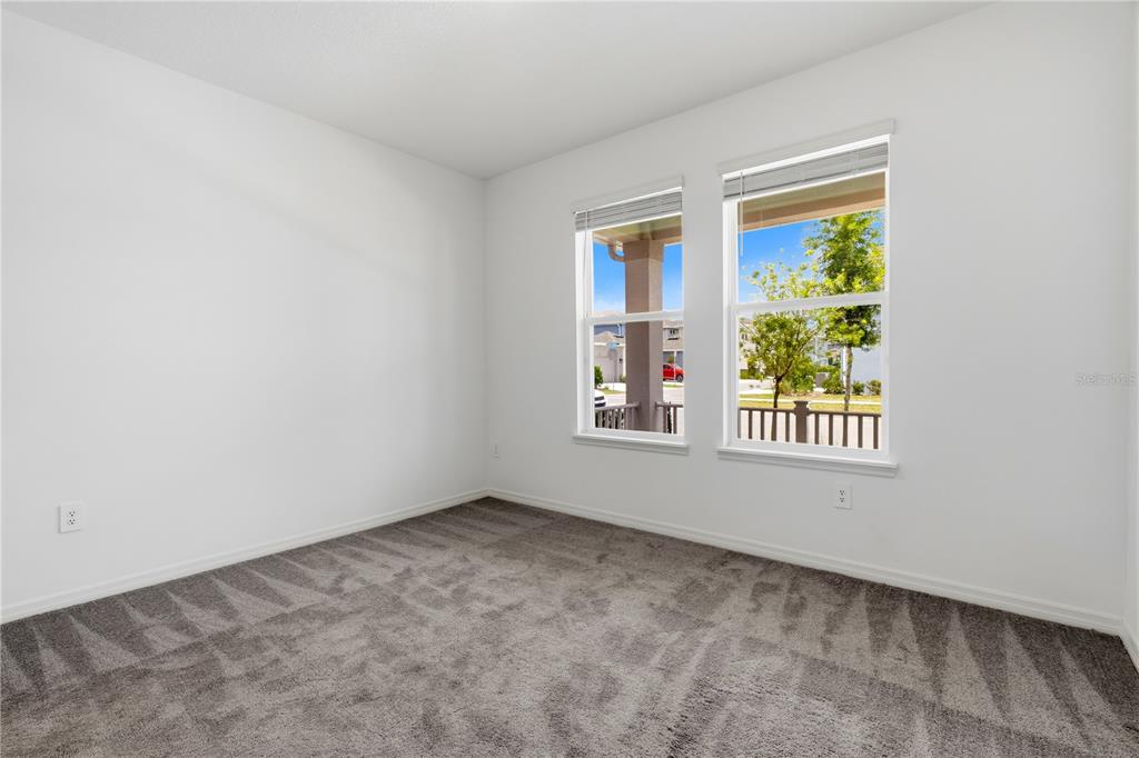 An empty bedroom features white walls, gray carpeting, and two windows overlooking a porch — 15010 SUMMER HARVEST STREET, WINTER GARDEN, FL