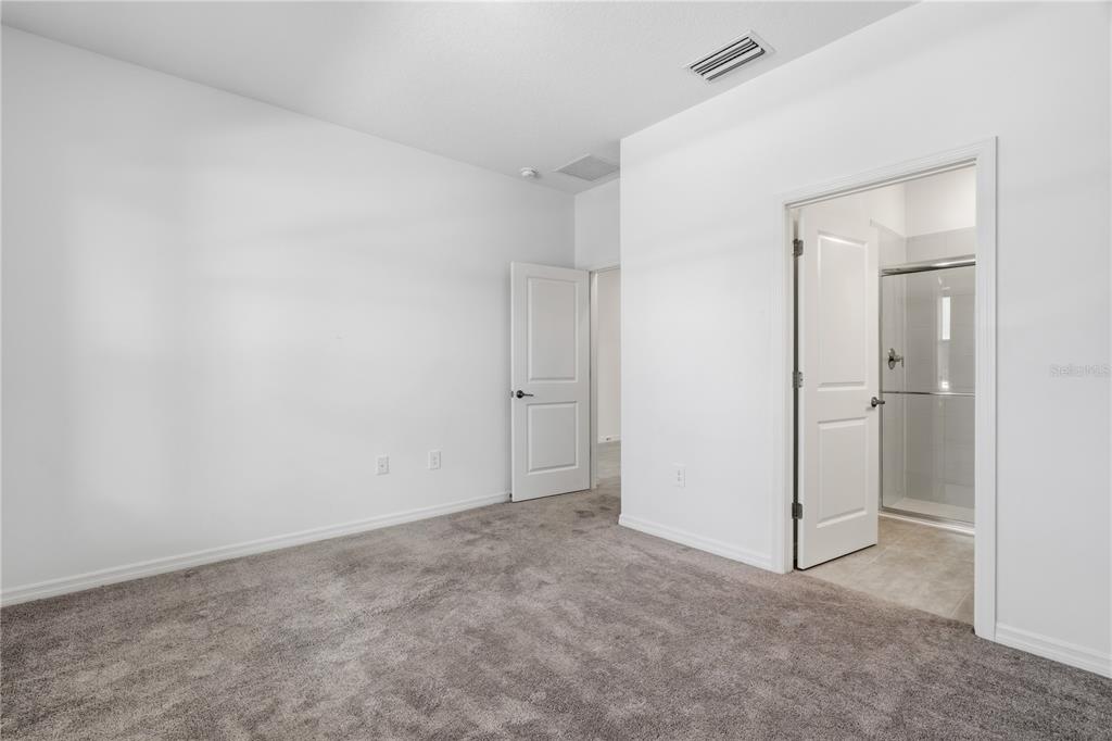 A bedroom with gray carpet, white walls, and an attached bathroom with a glass shower — 15010 SUMMER HARVEST STREET, WINTER GARDEN, FL