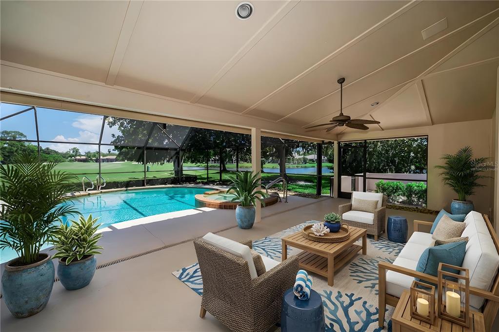 A covered patio features outdoor furniture, a swimming pool, and a view of a golf course — 4995 CAMBERLEY LANE, OLDSMAR, FL
