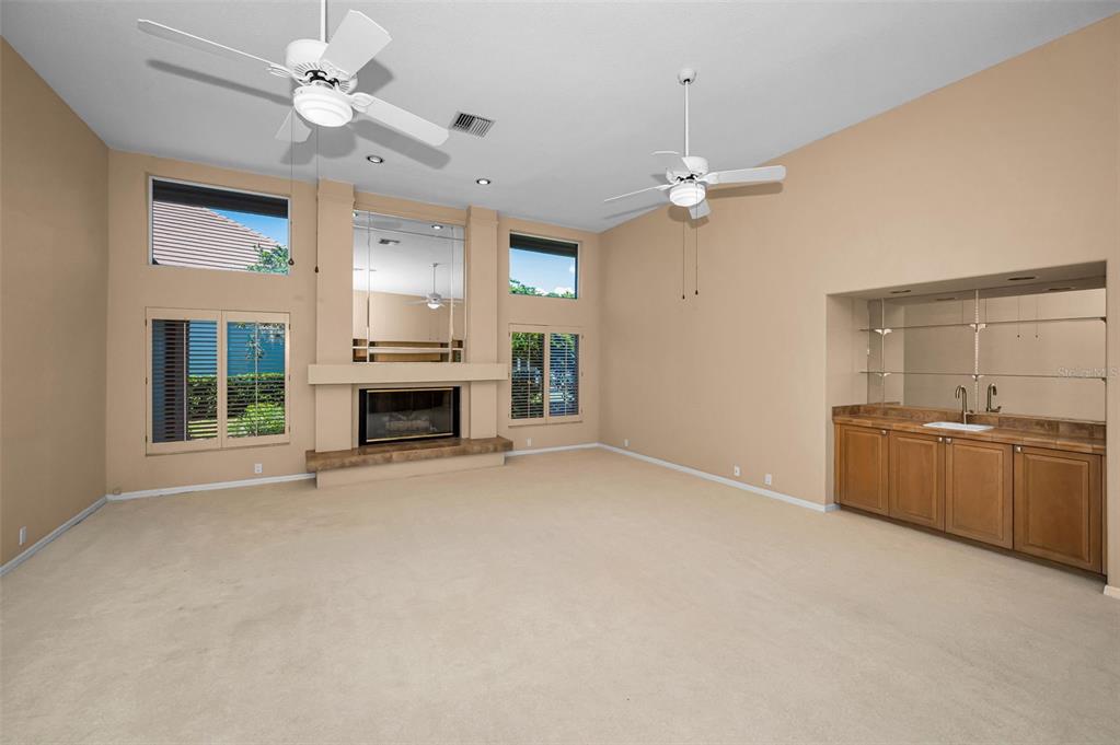 A living room features a fireplace, a wet bar, beige carpeting, and two ceiling fans — 4995 CAMBERLEY LANE, OLDSMAR, FL