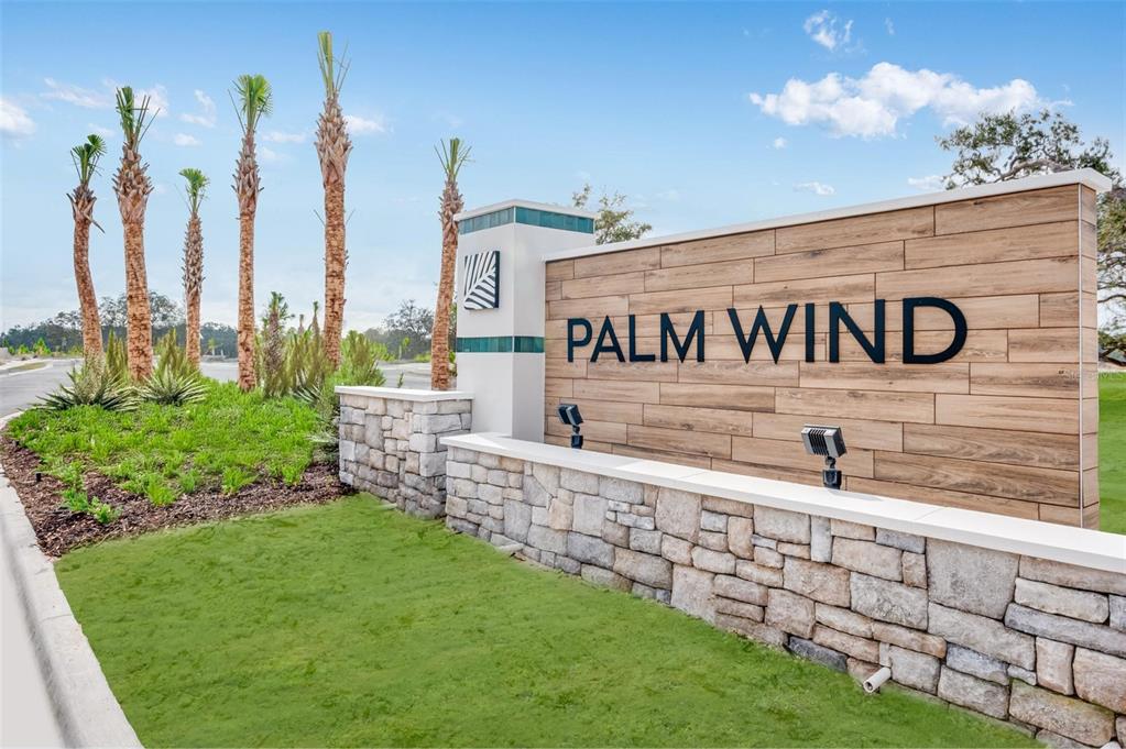 A stone and wood sign for Palm Wind stands in a landscaped residential area — 13626 TROPICAL BREEZE WAY, HUDSON, FL