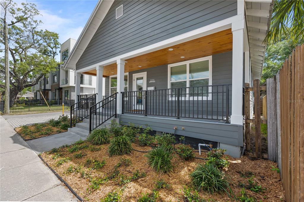 A gray house with a wooden porch ceiling and black metal railings sits near a sidewalk — 2203 N BOULEVARD, TAMPA, FL