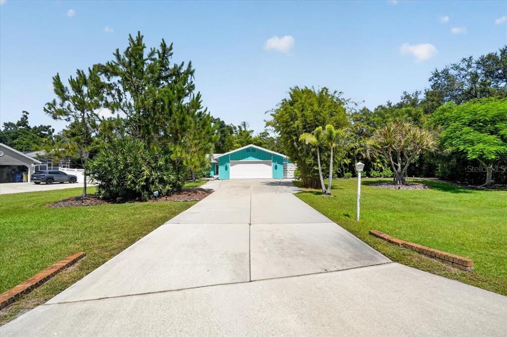 A teal house with a white garage door sits at the end of a long driveway — 3282 TOBERO LANE, SARASOTA, FL