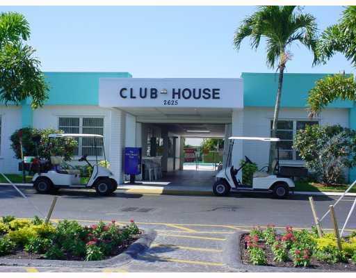 A clubhouse exterior with two parked golf carts and palm trees under a clear sky — 2556 E Dudley Dr Drive E # D, West Palm Beach FL 33415, WEST PALM BEACH, FL