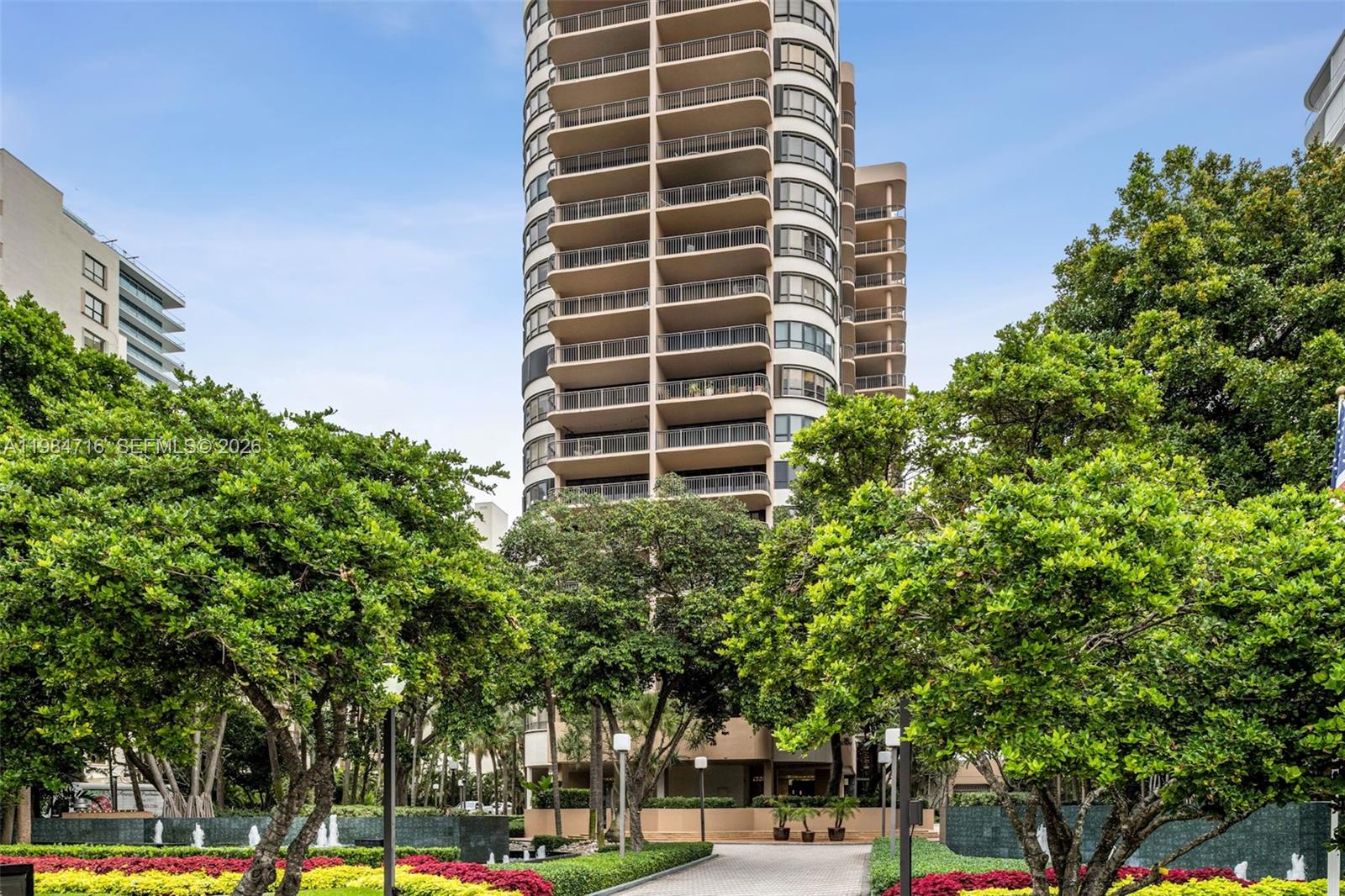 A tall residential high-rise building stands behind a landscaped garden with trees and walkways — 10175 Collins Ave # 807, Bal Harbour FL 33154, BAL HARBOUR, FL
