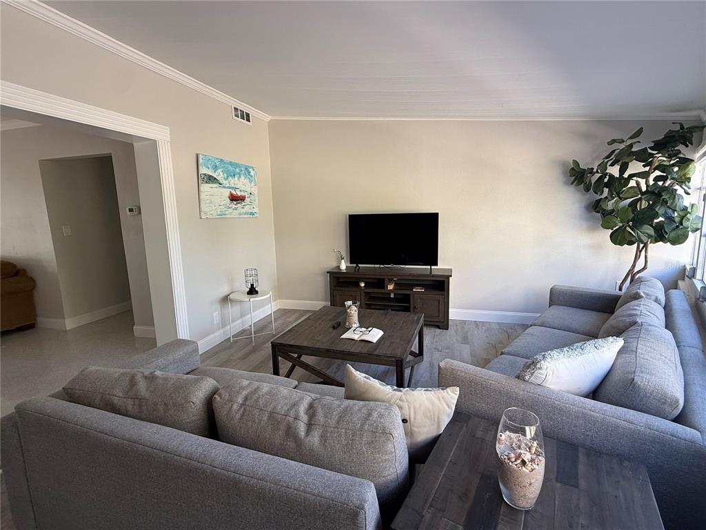 A living room features gray sofas, a wooden coffee table, and a television on a stand — 6407 1ST PALM POINT, ST PETE BEACH, FL