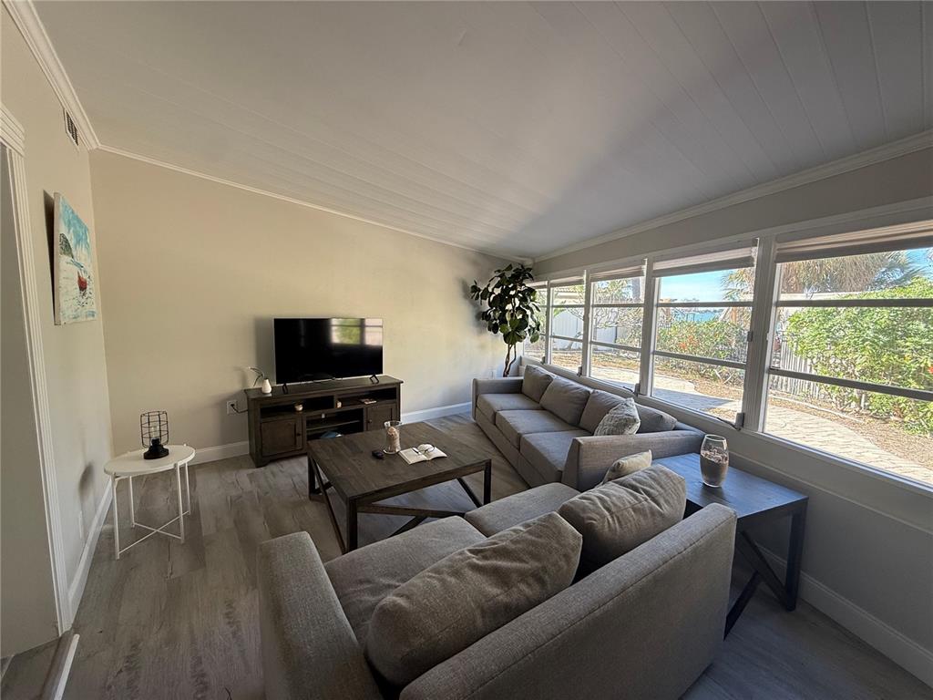 A living room features gray sofas, a wood coffee table, and large windows with outdoor views — 6407 1ST PALM POINT, ST PETE BEACH, FL