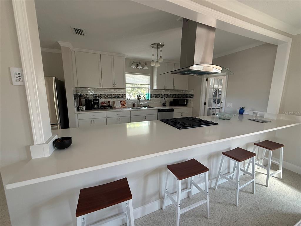A kitchen features white cabinets, a breakfast bar with three stools, and a gas cooktop — 6407 1ST PALM POINT, ST PETE BEACH, FL