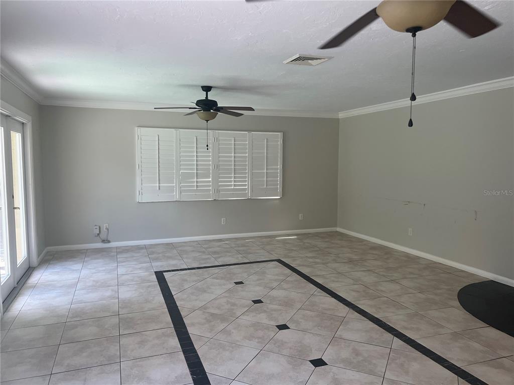 An empty room features light-colored tile flooring with a black decorative border and ceiling fans — 226 DELMAR AVE, SARASOTA, FL