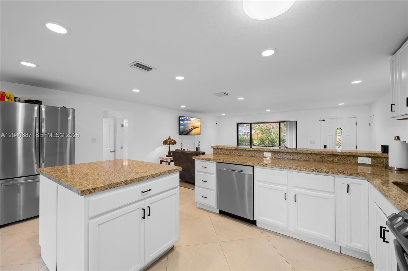 A kitchen with white cabinets and granite countertops opens into a living room area — 6839 Tradewind Way, Lake Worth FL 33462, LAKE WORTH, FL