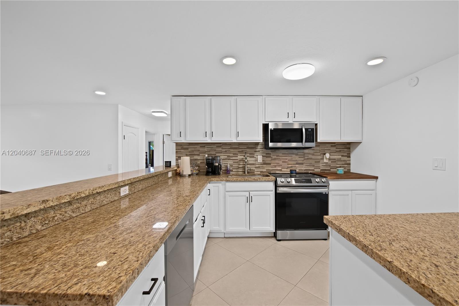 A kitchen features white cabinets, granite countertops, a center island, and stainless steel appliances — 6839 Tradewind Way, Lake Worth FL 33462, LAKE WORTH, FL