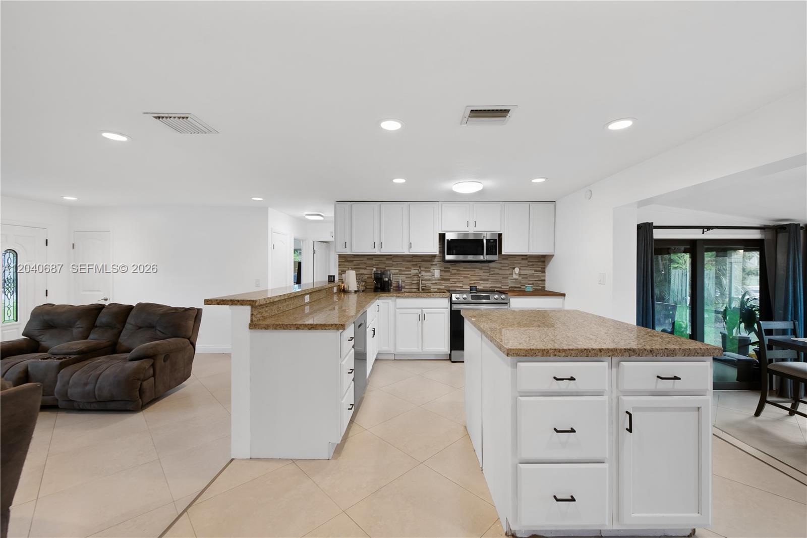 A kitchen features white cabinets, granite countertops, stainless steel appliances, and a tiled backsplash — 6839 Tradewind Way, Lake Worth FL 33462, LAKE WORTH, FL