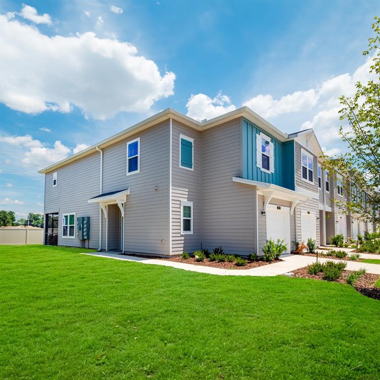 A two-story townhouse with gray siding, blue accents, and a green lawn under a sky — 3868 SE 36TH LANE, OCALA, FL