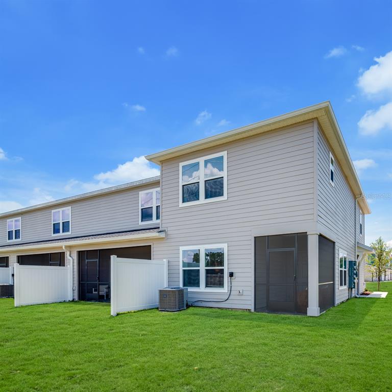 The rear exterior of a two-story townhouse features gray siding, screened lanais, and white fencing — 3868 SE 36TH LANE, OCALA, FL