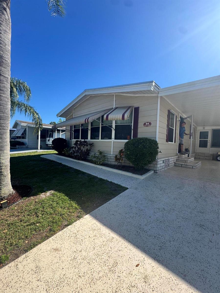 A tan manufactured home with a carport, striped awnings, and a small front garden — 54 Calle De Lagos, Fort Pierce FL 34951, FORT PIERCE, FL