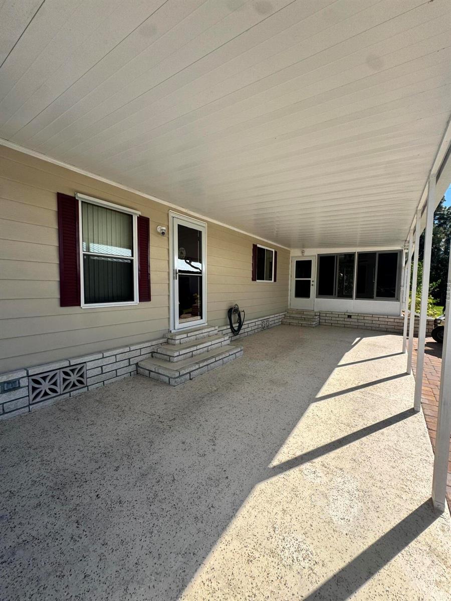 A covered concrete patio area features light siding, brick skirting, and two entry doors — 54 Calle De Lagos, Fort Pierce FL 34951, FORT PIERCE, FL