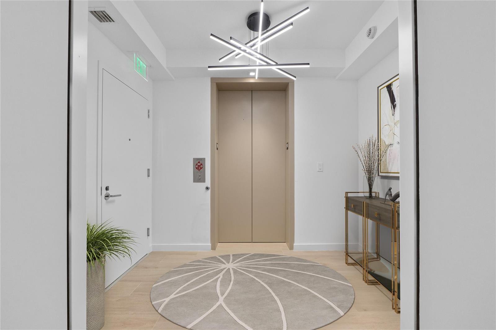 A modern elevator lobby features a geometric light fixture, a round patterned rug, and console table — 1116 N Ocean Boulevard # 904, Pompano Beach FL 33062, POMPANO BEACH, FL