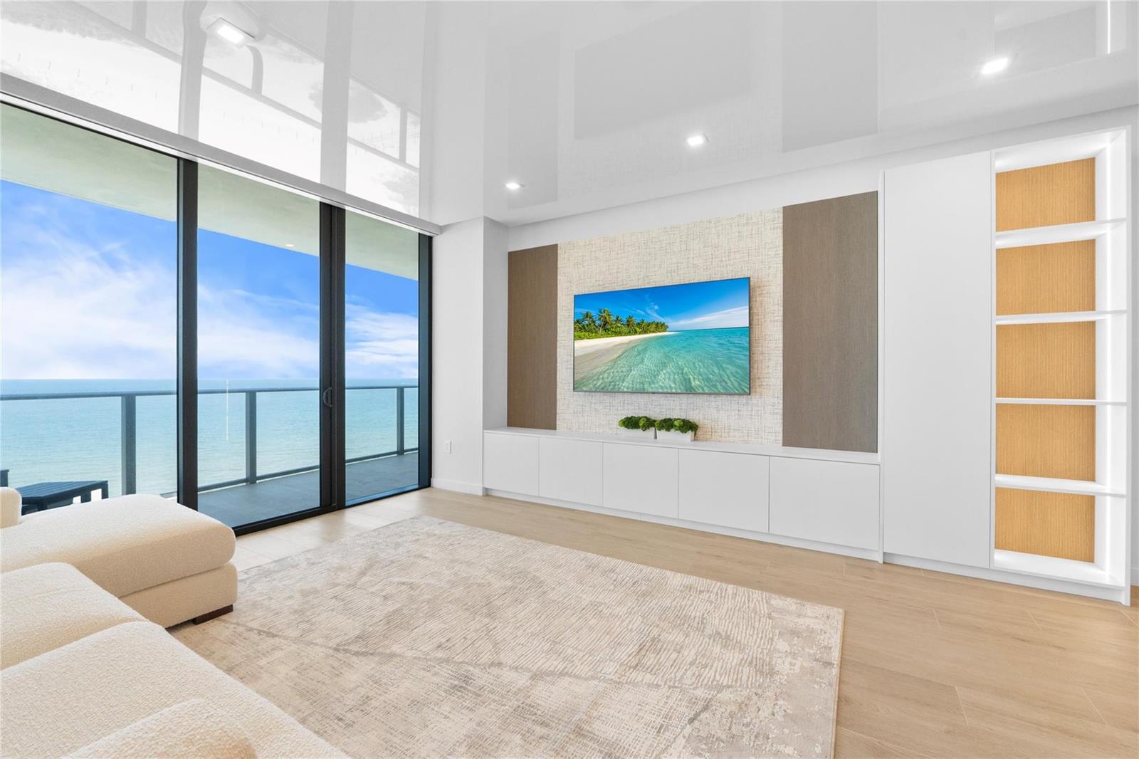 A modern living room features a wall-mounted television, built-in cabinetry, and floor-to-ceiling ocean views — 1116 N Ocean Boulevard # 904, Pompano Beach FL 33062, POMPANO BEACH, FL