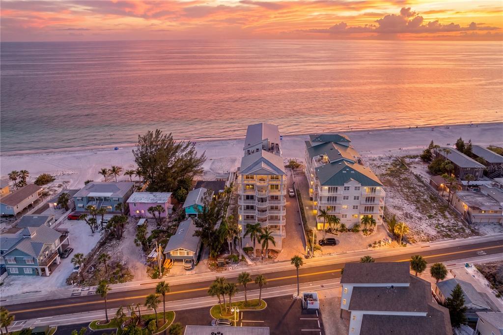 An aerial view shows beachfront condominiums and houses along a road at sunset — 19730 GULF BOULEVARD UNIT 400, INDIAN ROCKS BEACH, FL
