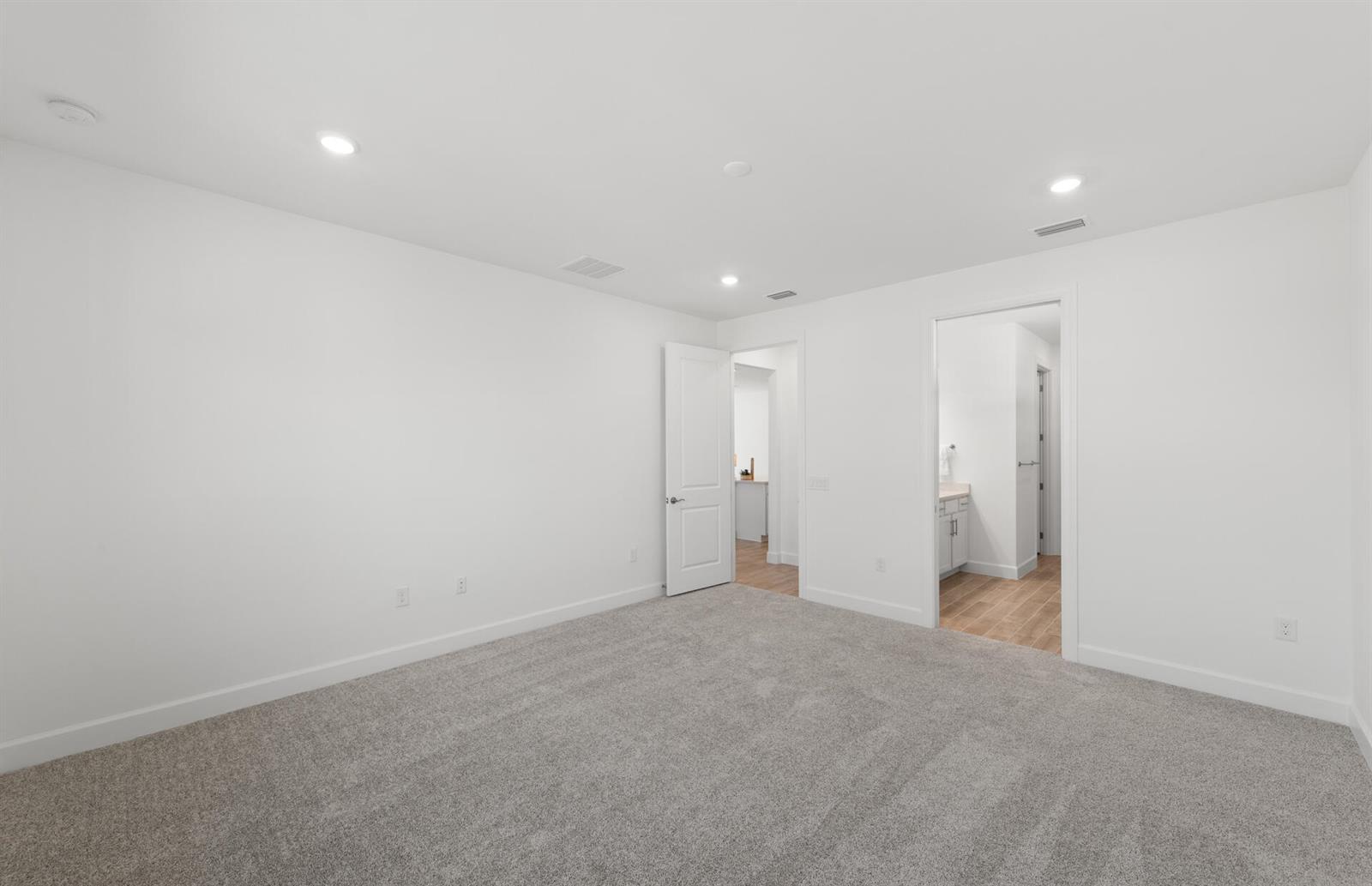 A bright, empty bedroom features white walls, gray carpeting, and two doorways leading to other rooms — 12584 Quartz Drive, FL 33920, FL