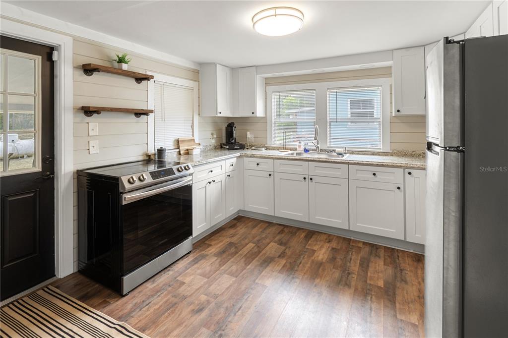 A kitchen features white cabinets, dark wood-look flooring, a black stove, and open shelving — 301 WEAVER AVENUE, LAKE WALES, FL
