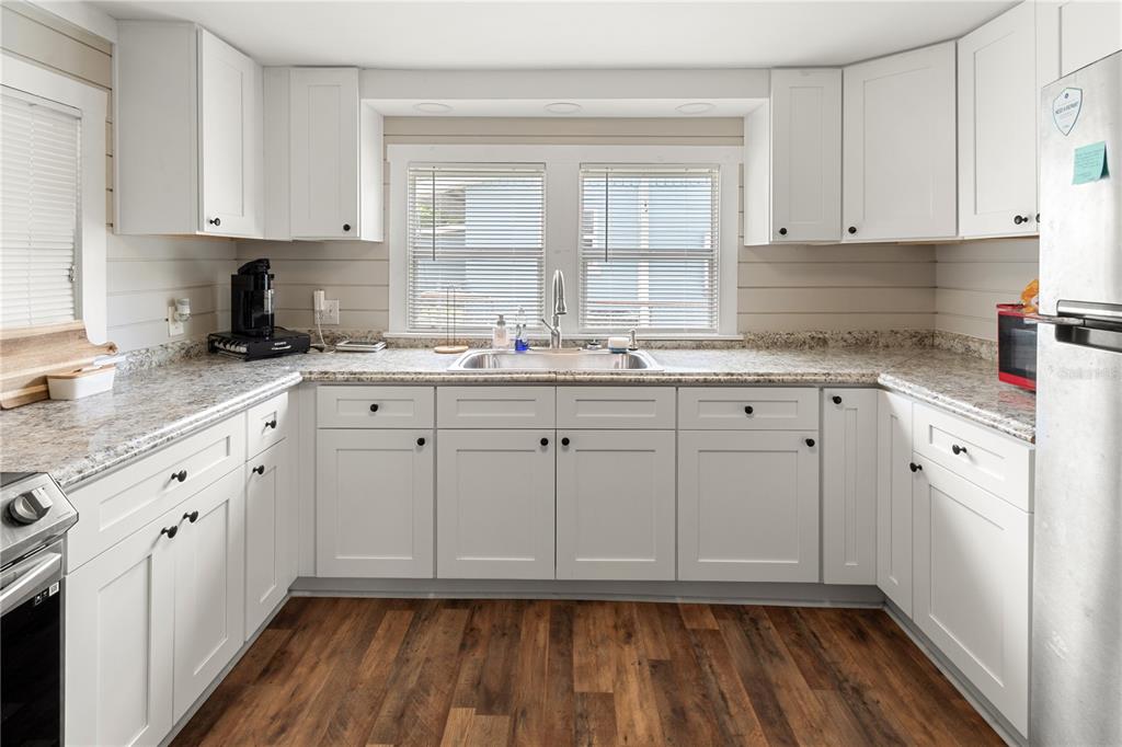 A kitchen features white cabinets, granite countertops, a stainless steel sink, and wood-look flooring — 301 WEAVER AVENUE, LAKE WALES, FL