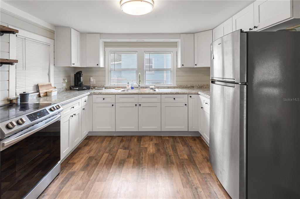 A kitchen features white cabinets, granite countertops, stainless steel appliances, and wood-look flooring — 301 WEAVER AVENUE, LAKE WALES, FL