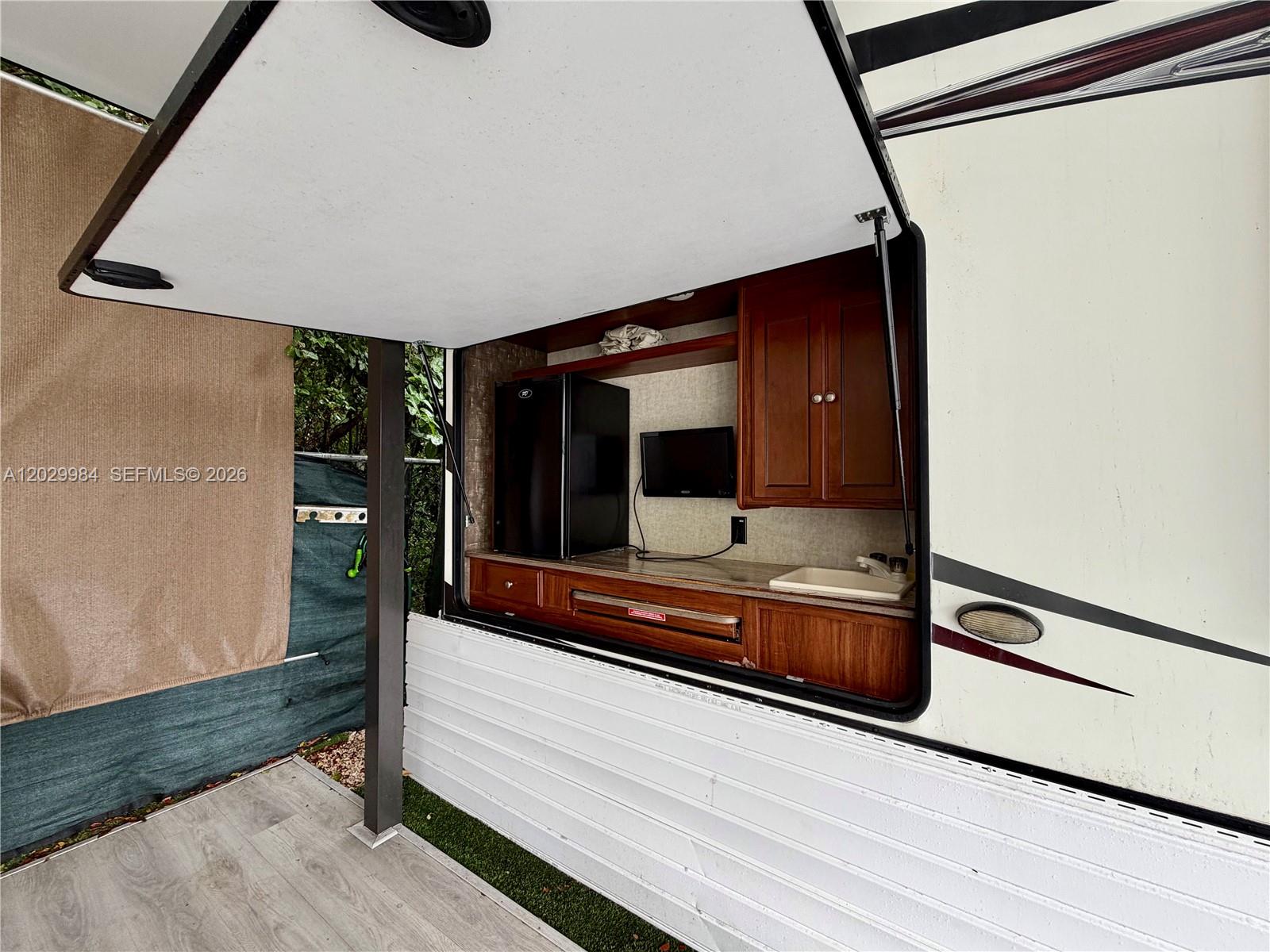 An outdoor RV kitchen features a small refrigerator, sink, cabinets, and a mounted television — 325 Calusa St #122, Key Largo FL 33037, KEY LARGO, FL