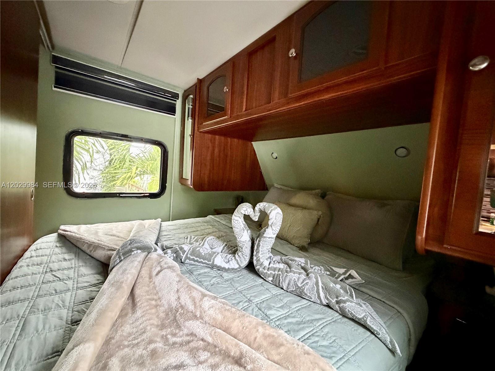 A bedroom in a recreational vehicle features a bed with towel swans and wooden cabinetry — 325 Calusa St #122, Key Largo FL 33037, KEY LARGO, FL