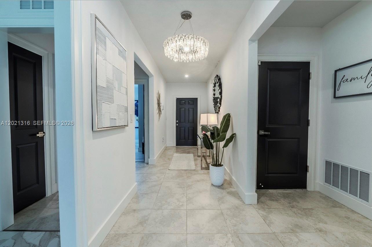 A bright hallway features white walls, tiled floors, black doors, and a crystal chandelier — 215 Raspberry Rd, Fort Pierce FL 34981, FORT PIERCE, FL