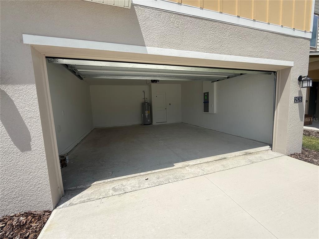 An open, empty two-car garage with a concrete floor and a water heater — 2528 ABSOLUTE AVENUE, HAINES CITY, FL