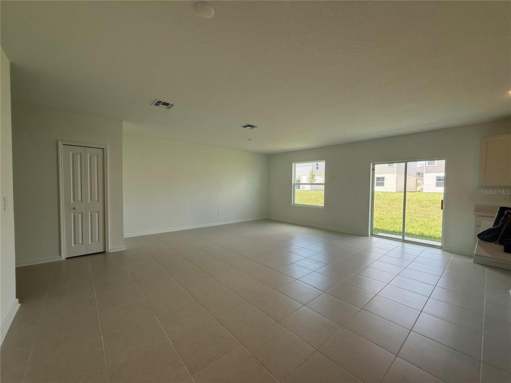 An open-concept living area features light-colored tile flooring, white walls, and a sliding glass door — 2528 ABSOLUTE AVENUE, HAINES CITY, FL