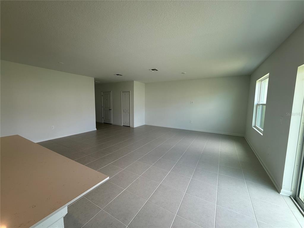 An open-concept living area features light-colored tile flooring, white walls, and a kitchen counter — 2528 ABSOLUTE AVENUE, HAINES CITY, FL