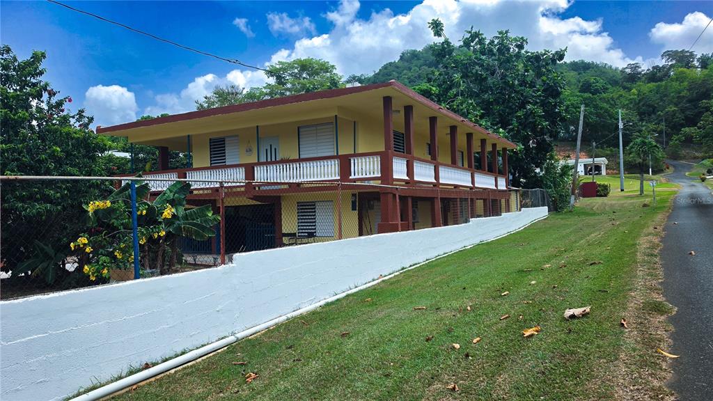 A two-story yellow house with a wrap-around balcony sits behind a white concrete wall — carr. 985 km 3.0 BO. FLORENCIO, FAJARDO, PR