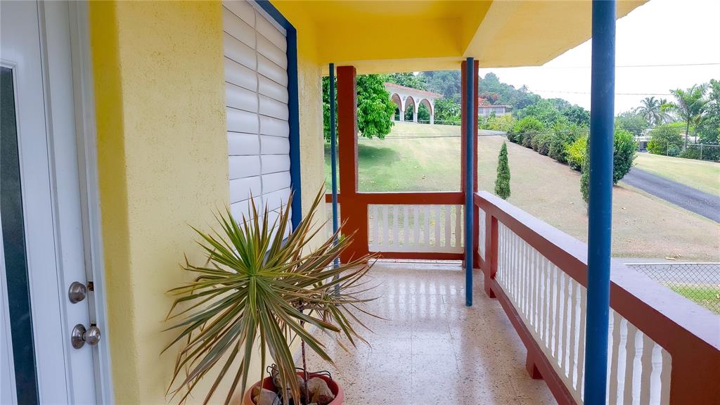 A yellow-walled balcony features a potted plant, blue support columns, and a white railing — carr. 985 km 3.0 BO. FLORENCIO, FAJARDO, PR