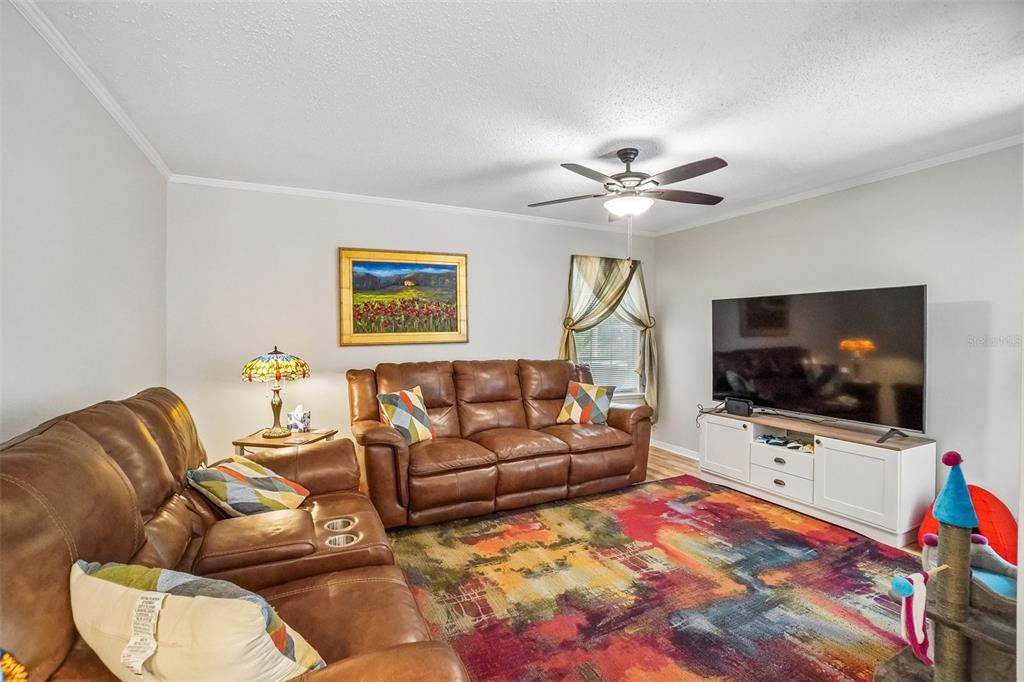 A living room features brown leather sofas, a colorful area rug, and a television console — 8350 SAVANNAH TRACE CIRCLE UNIT 1601, TAMPA, FL