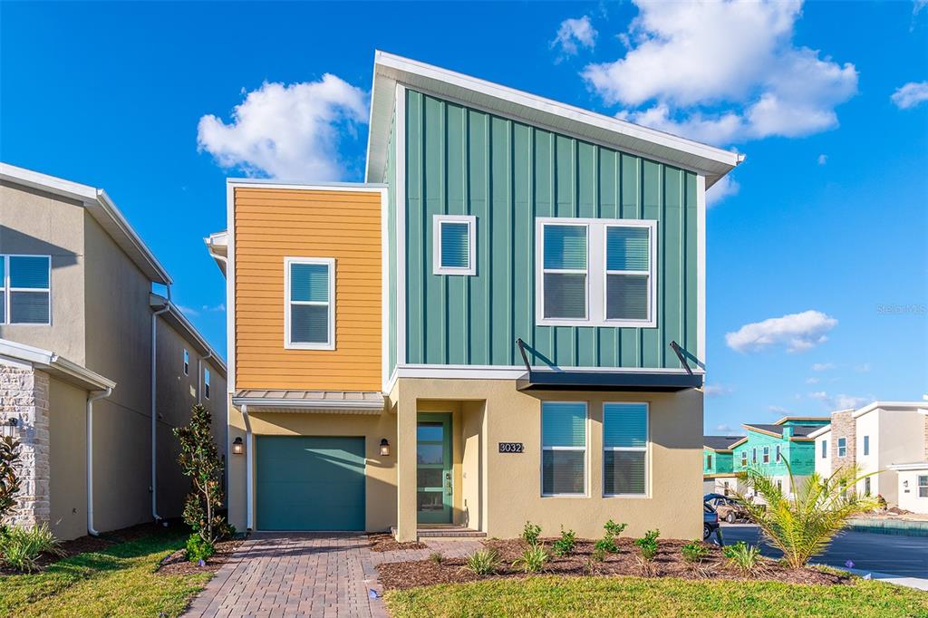 A modern two-story house features a teal metal-sided upper level, yellow stucco, and a garage — 3032 PROTAGONIST STREET, KISSIMMEE, FL