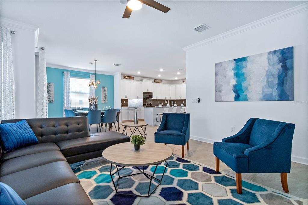 An open-concept living room features a grey sectional, blue accent chairs, and a geometric rug — 3032 PROTAGONIST STREET, KISSIMMEE, FL