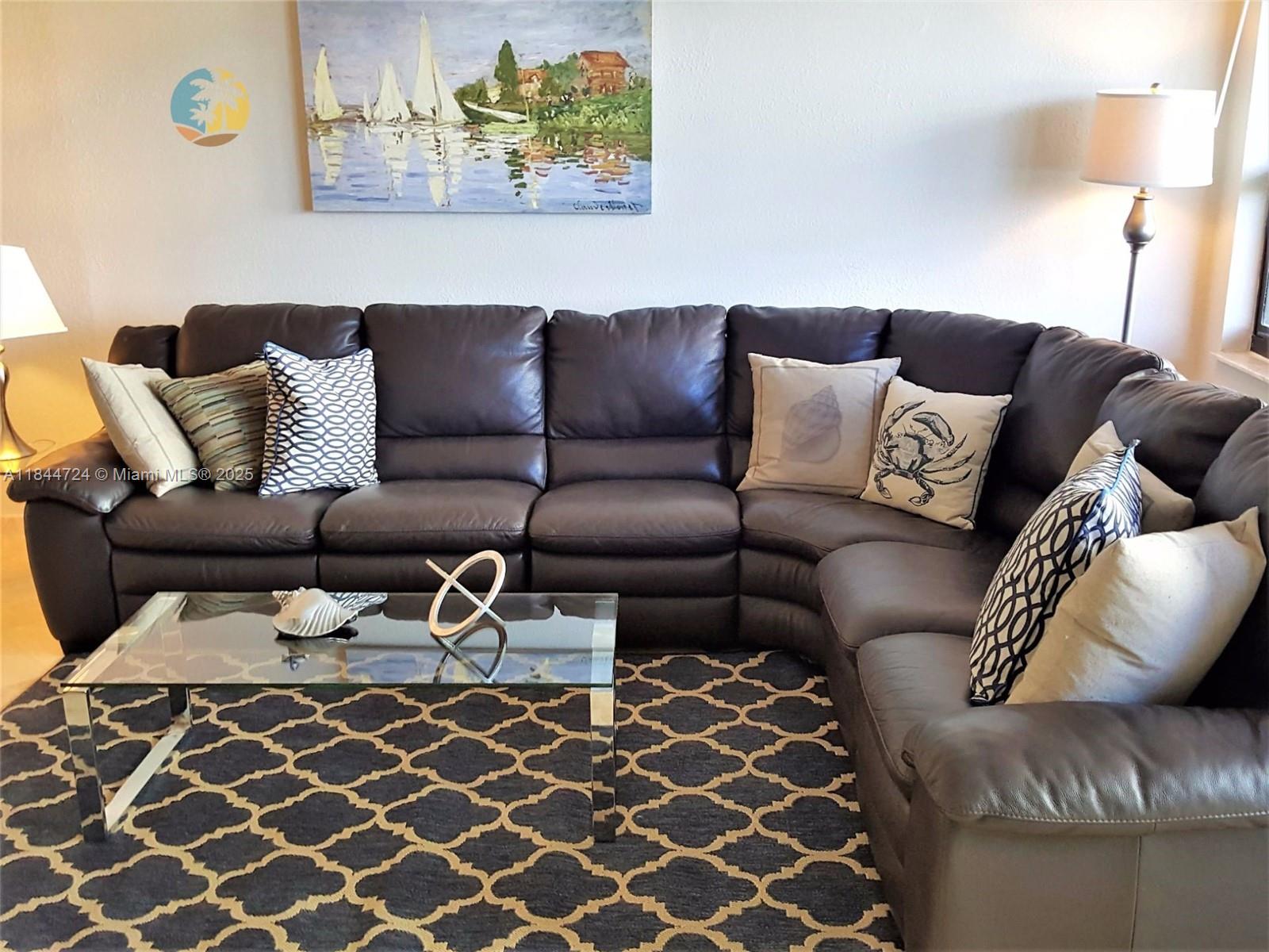 A living room features a dark leather sectional sofa, a glass coffee table, and patterned rug — 5225 Collins Ave # 510, Miami Beach FL 33140, MIAMI BEACH, FL