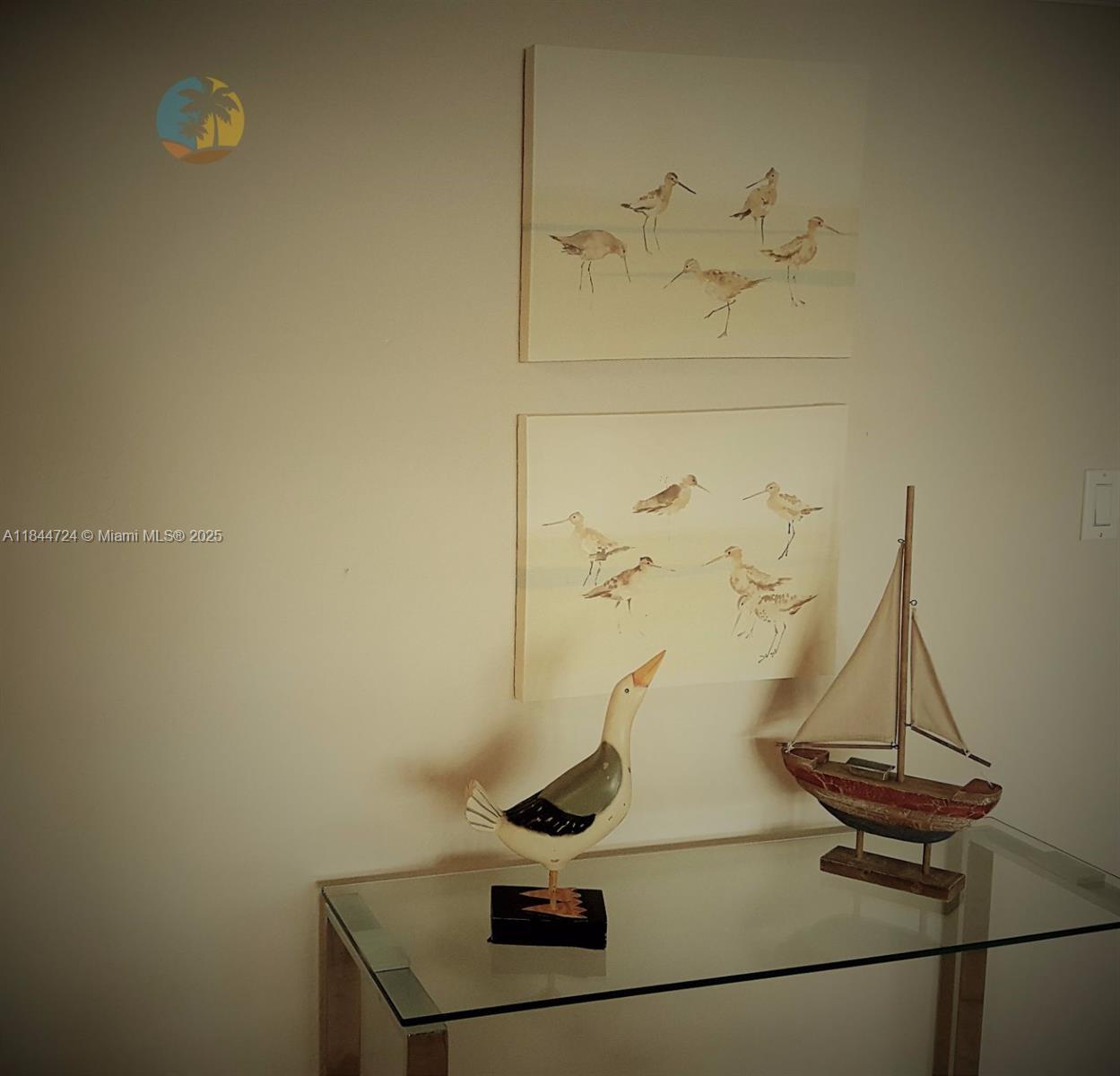 A glass console table displays a bird figurine and a model sailboat beneath two bird paintings — 5225 Collins Ave # 510, Miami Beach FL 33140, MIAMI BEACH, FL