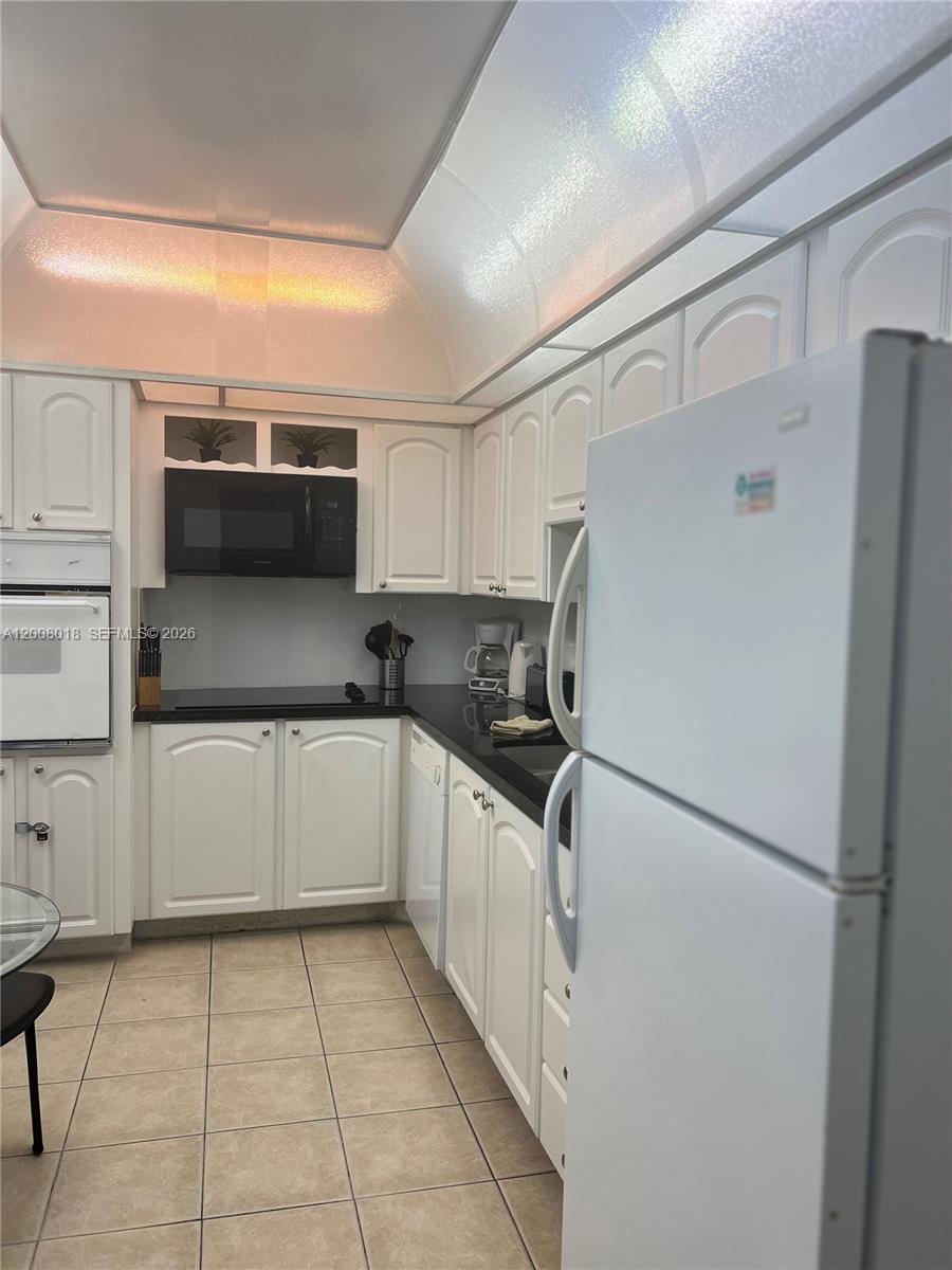 A kitchen features white cabinetry, black countertops, a white refrigerator, and a vaulted ceiling — 3901 S Ocean Dr # 14T, Hollywood FL 33019, HOLLYWOOD, FL